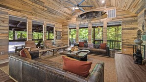 A rustic cabin interior with wooden walls, a ceiling fan, large windows, and a leather couch.
