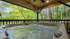 A hot tub with a wooden deck and a view of a forest.