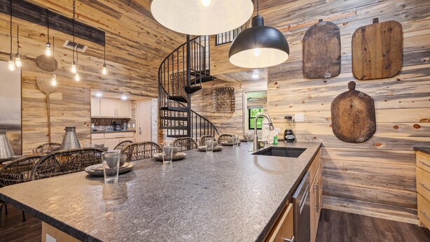 A kitchen with a central island, wooden walls, a black spiral staircase, and hanging wooden boards.