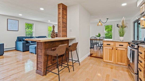 Een moderne keuken met houten kastjes, een centraal eiland met barkrukken, en een zithoek met stoelen.
