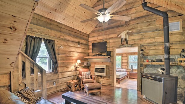 A cozy cabin interior with a wooden interior, a sofa, a chair, a fireplace, and a television.