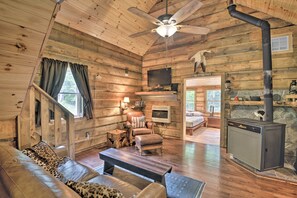 Un intérieur de chalet chaleureux, avec un revêtement mural en bois, un canapé, un fauteuil, une cheminée et un téléviseur.