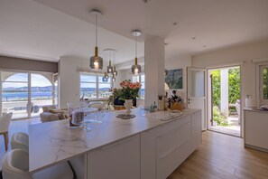 Una cocina moderna con una isla grande, luces colgantes y vistas al mar.