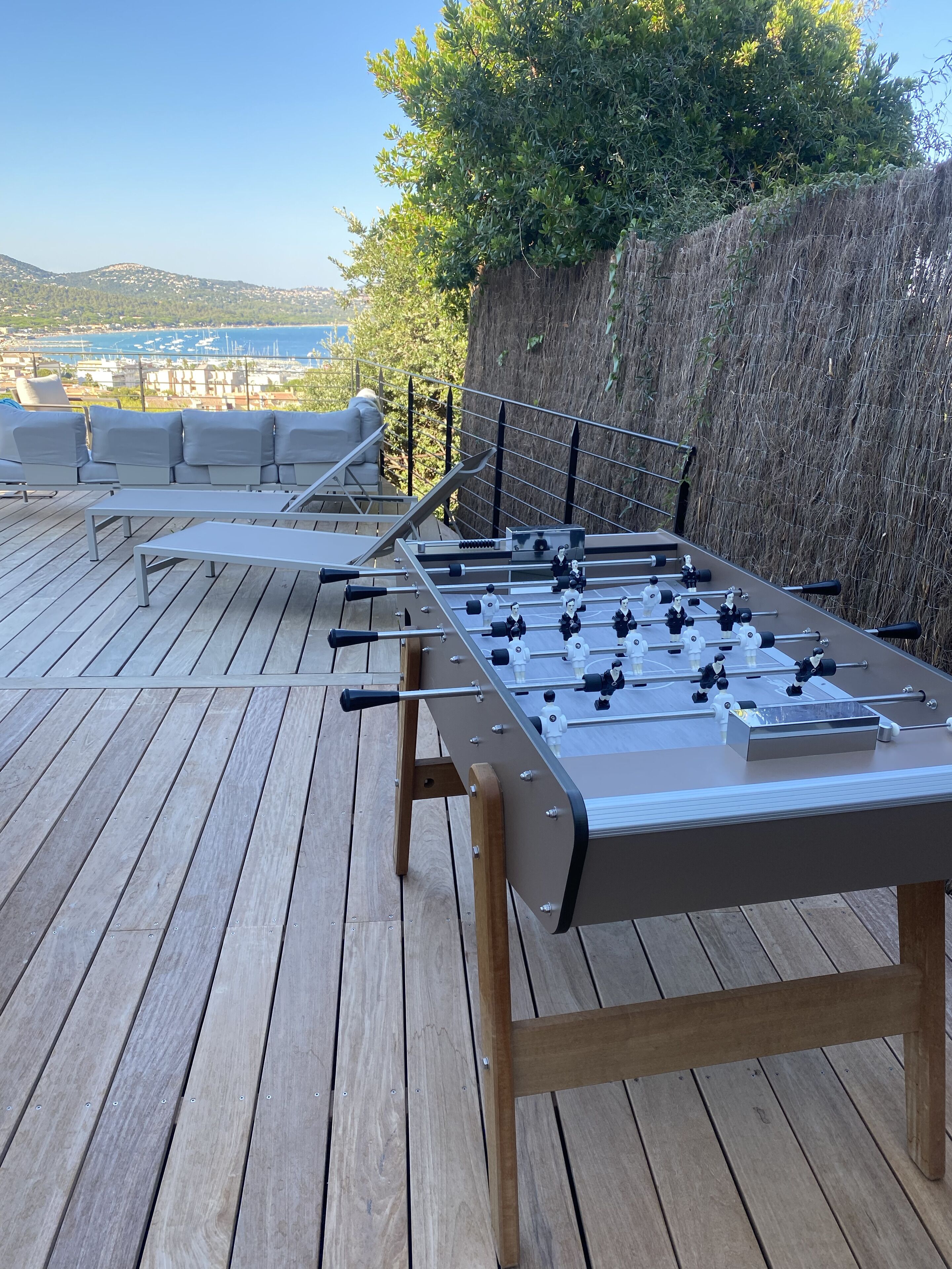 Ein Kicker auf einer Holzdiele mit Blick auf das Meer und Gebäude im Hintergrund.