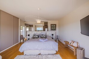 Un dormitorio con una cama grande, un banco de madera, una maleta y un televisor en la pared.