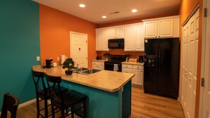 Una cocina con paredes verde azulado, gabinetes blancos, un refrigerador negro e isla de madera con taburetes de bar.