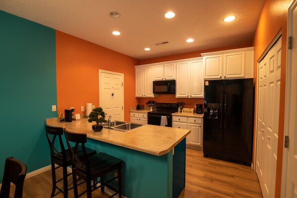 A kitchen with teal walls, white cabinets, a black refrigerator, and a wooden island with bar stools. - Golf Getaway - King Bed, Pool,  Minutes to Casino! (Mesquite)