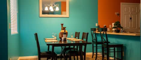 Zona pranzo con tavolo apparecchiato per quattro persone, sedie, lampadario e specchio a parete.