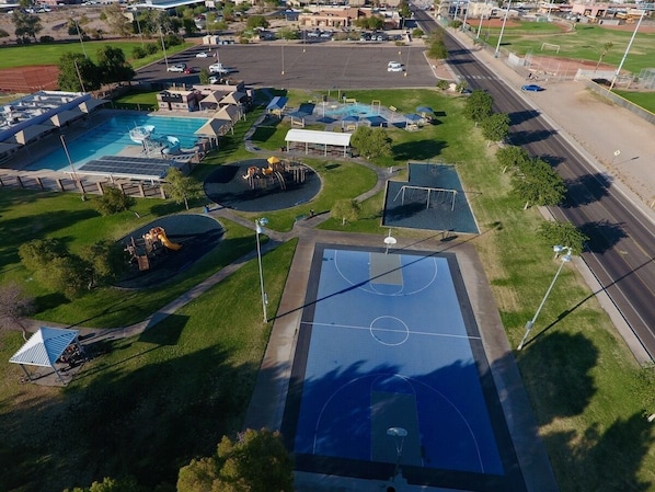 An aerial view of a sports complex with a basketball court, swimming pool, and playground.