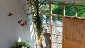 A room with a wooden ceiling, a large window with a view of greenery, a statue, and a patterned rug. - Vacation apartment with large panoramic window (Teisendorf)