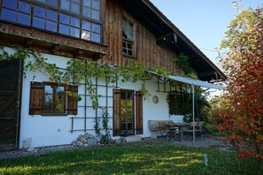 A rustic wooden house with a white exterior, large windows, and a covered patio area with outdoor seating.
