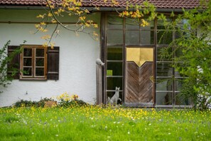 A rustic house with a white exterior, wooden shutters, and a large window.