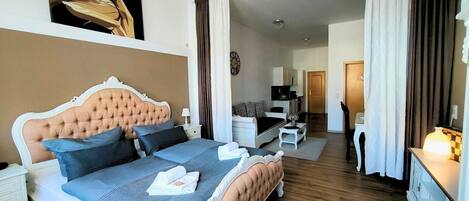 A bedroom with a large bed, a desk, a chair, a television, and a chandelier.
