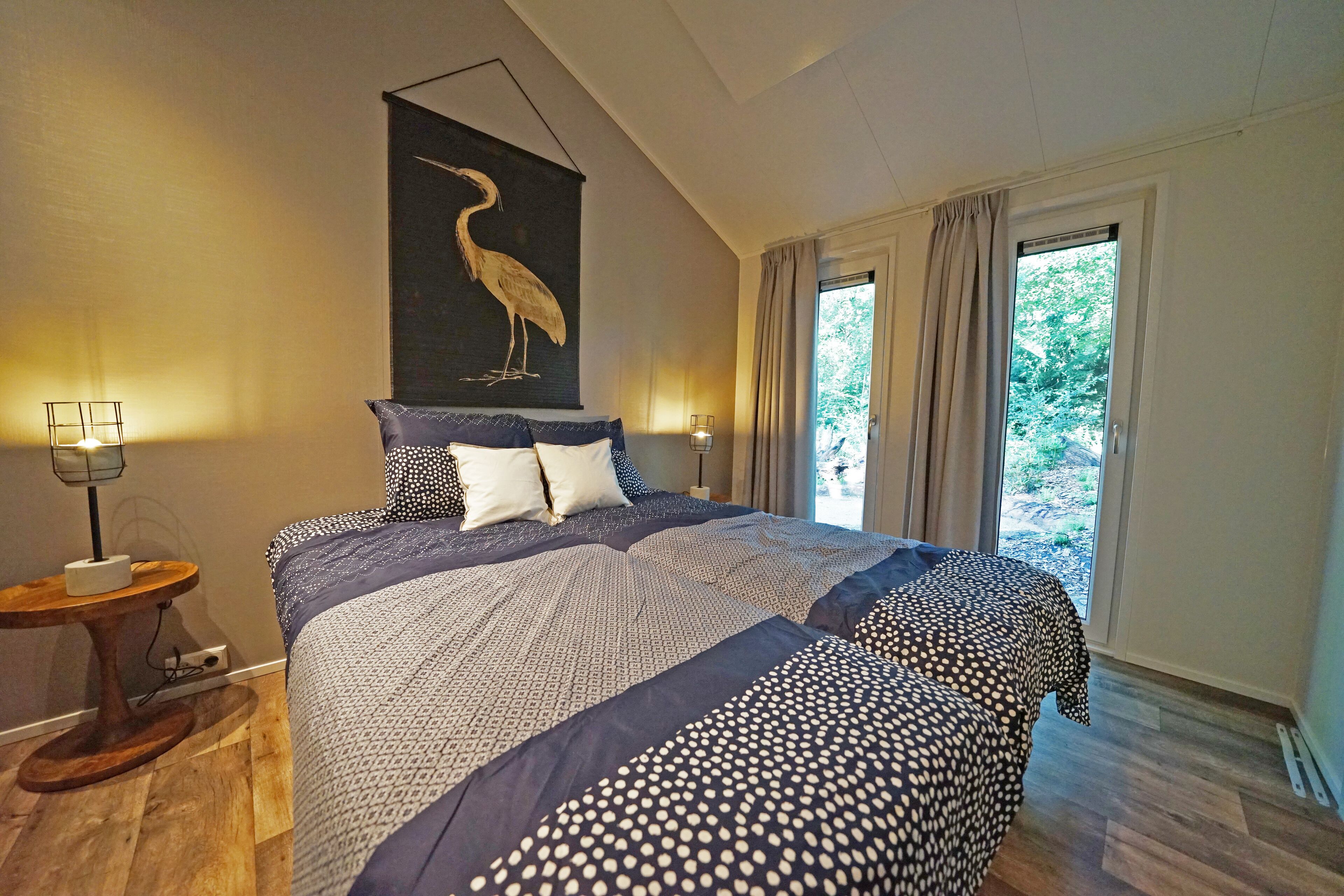 A bedroom with a large bed, a wooden floor, a wall-mounted artwork of a bird, and a window with curtains.