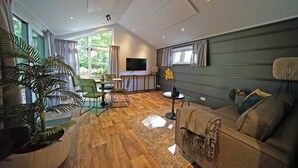 Una sala de estar moderna con piso de madera, un sofá, un televisor y un ventanal con cortinas.