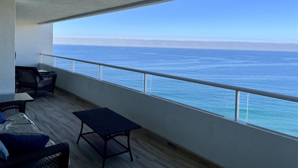 Varanda com vista para o oceano, mobiliada com mesa e cadeiras, e um corrimão.