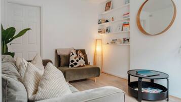 Un salon avec un canapé, une table d’appoint, une lampe et une bibliothèque.