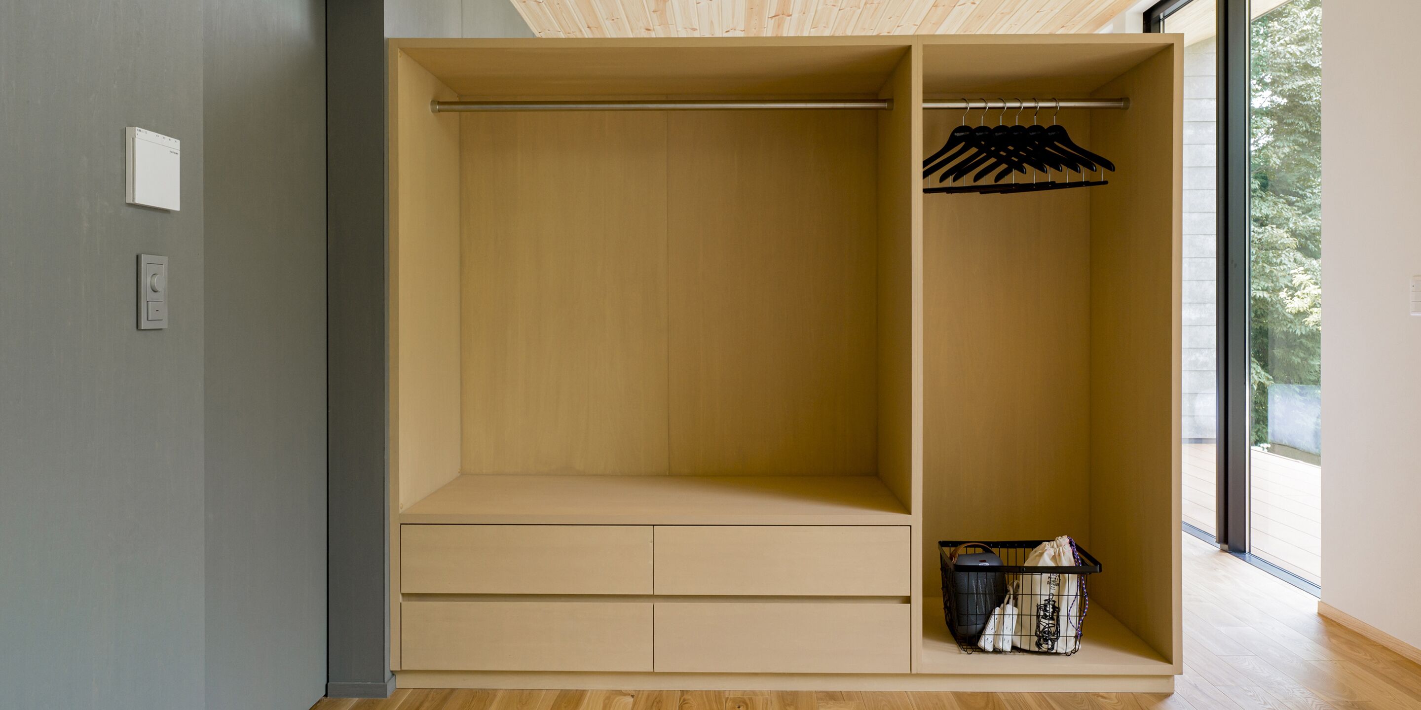 Un armario moderno con detalles de madera, una barra para colgar y una cesta con bolsos.