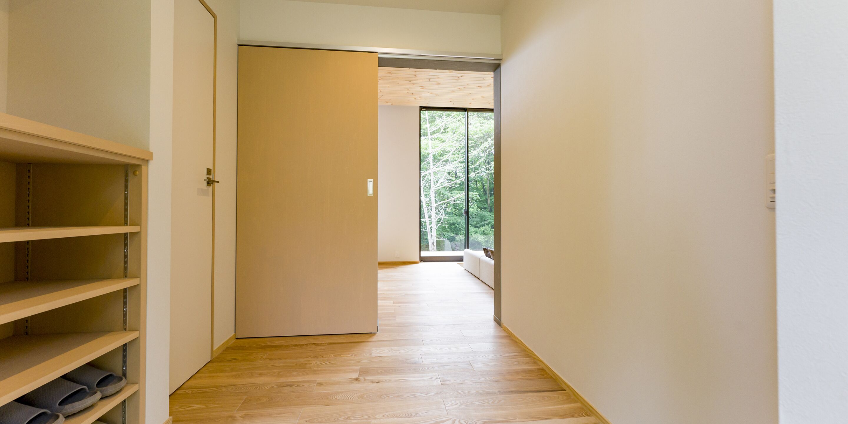 A hallway with wooden flooring, a sliding door, and a view of trees through a window.
