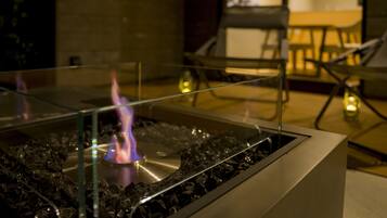 A glass-top table with a central flame, surrounded by chairs and a table in a dimly lit room.