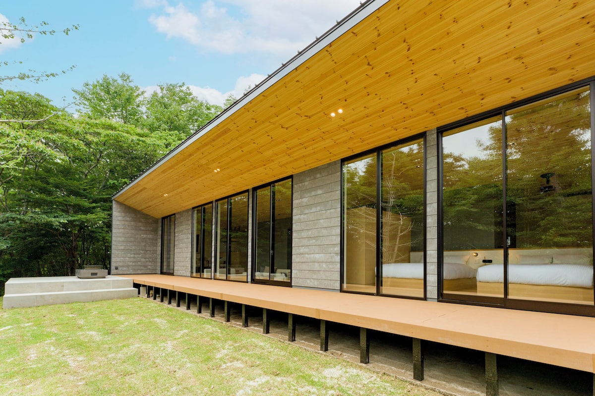 A modern building with a wooden roof, large glass windows, and a long bench outside.