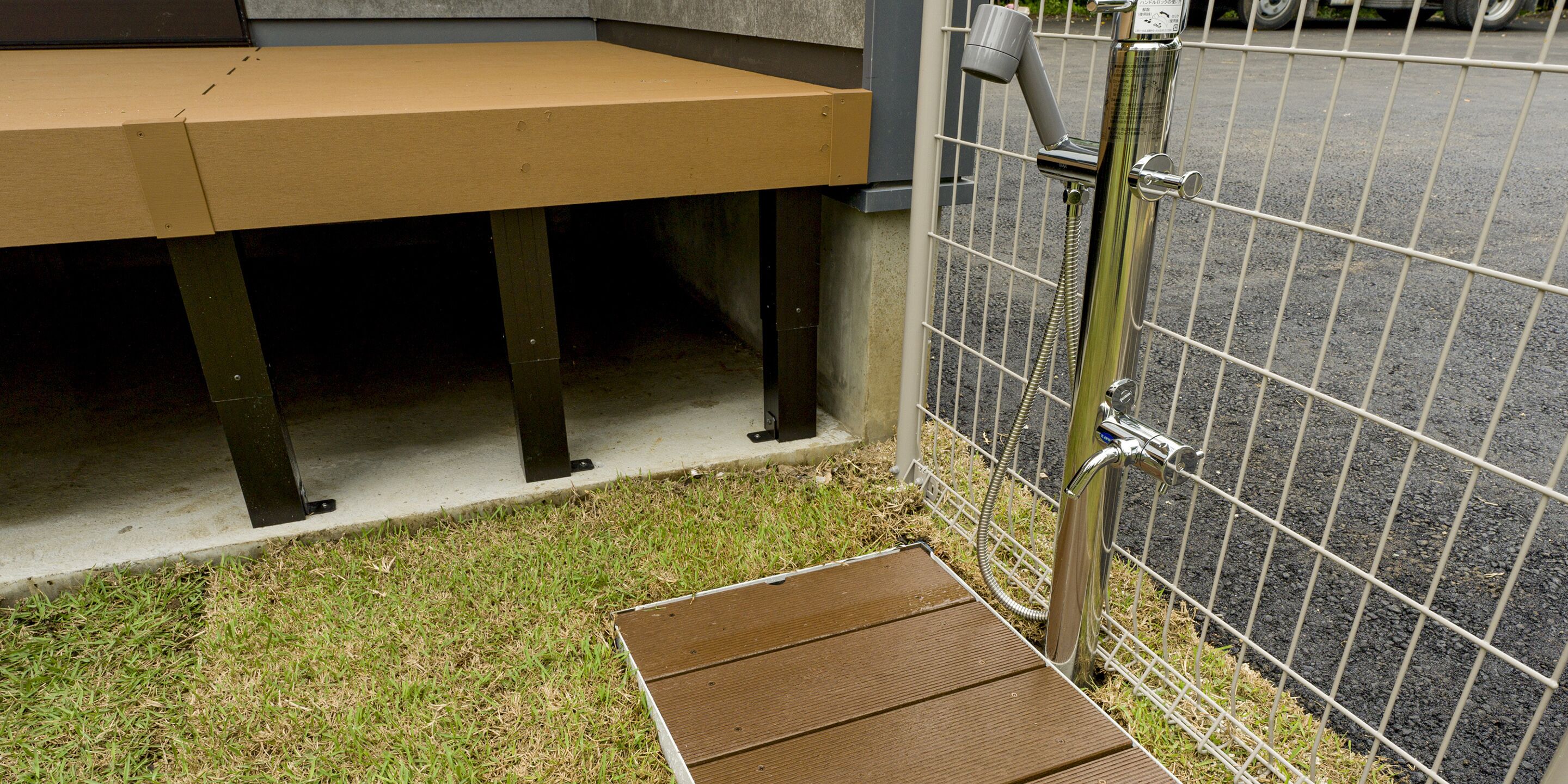 A metal fence, a concrete bench, and a metal hose attached to a wall.