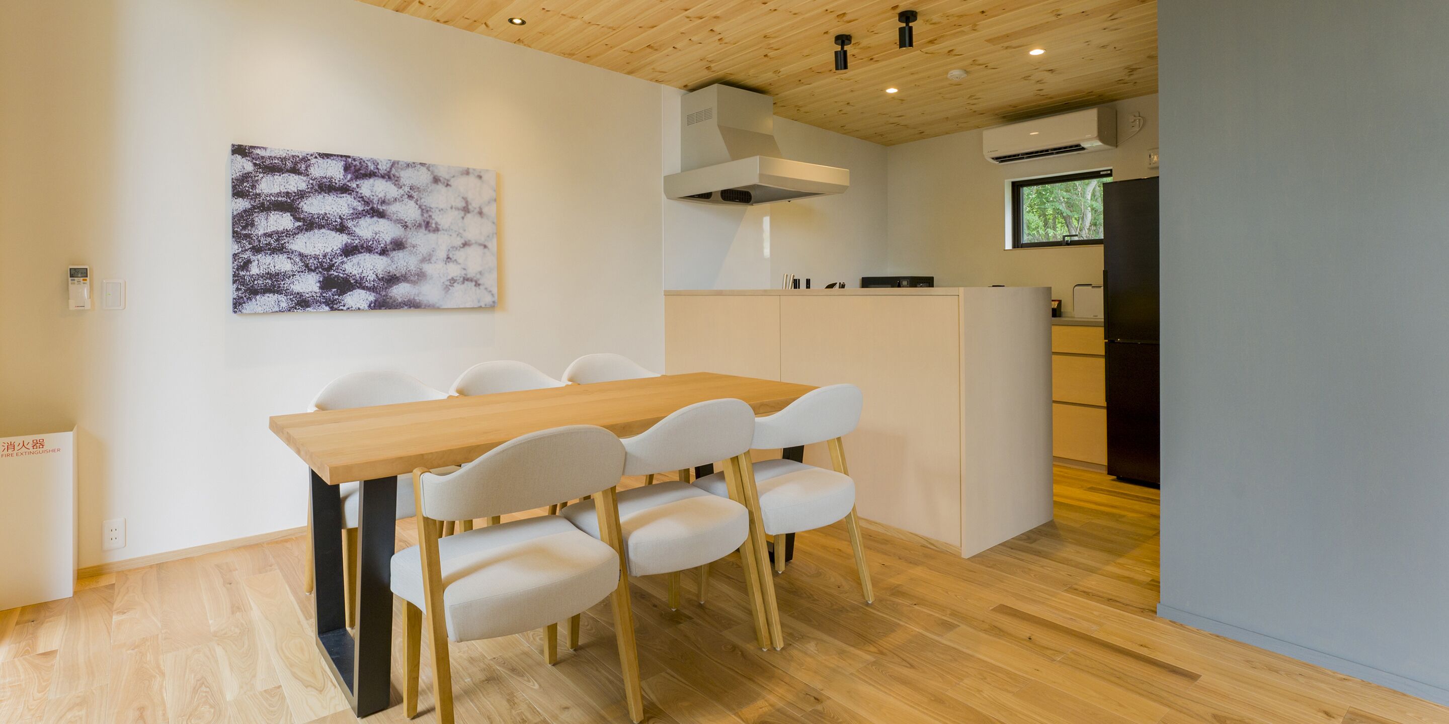 A modern kitchen with a wooden table and chairs, a white island, and a large window.