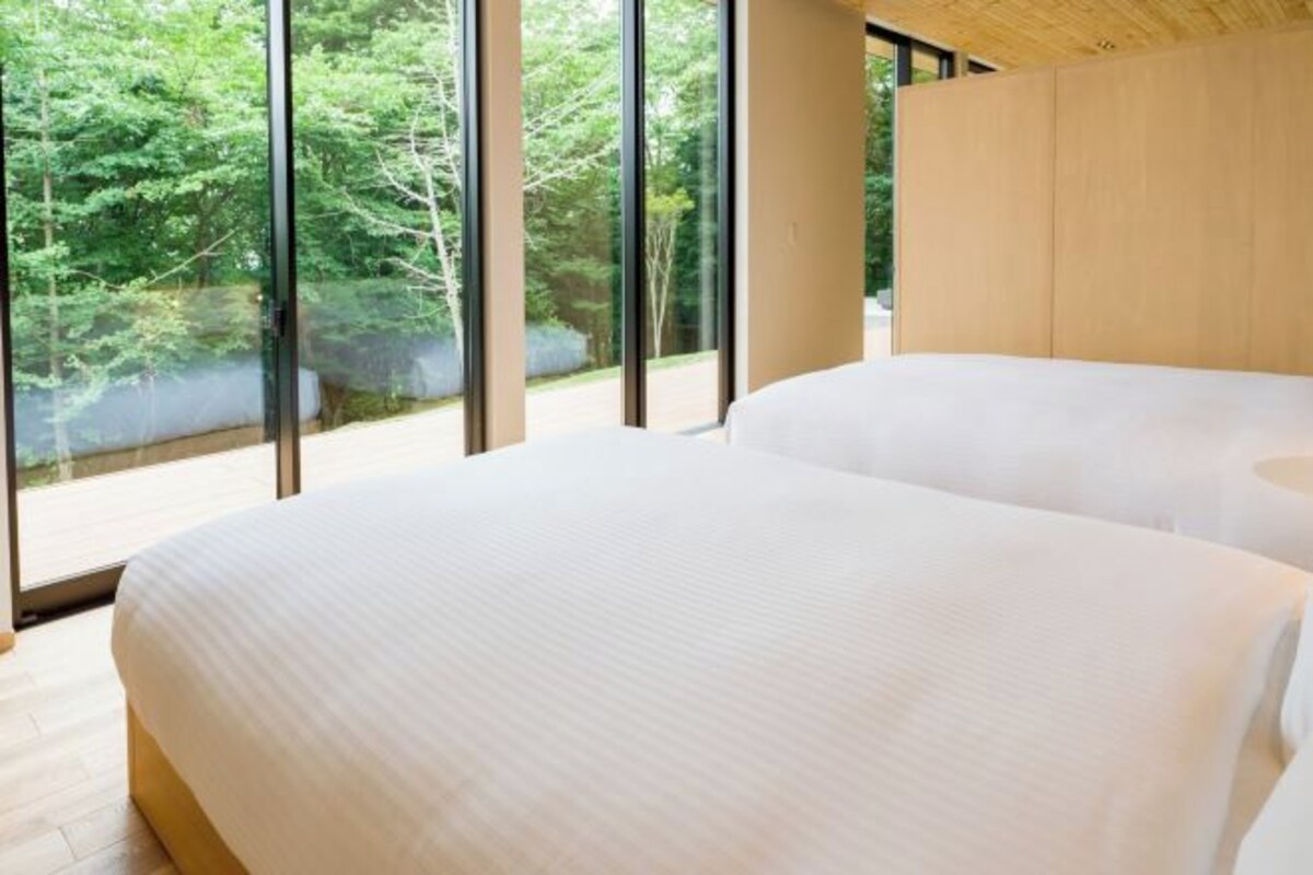 A modern bedroom with large windows, a bed, and a wooden headboard.