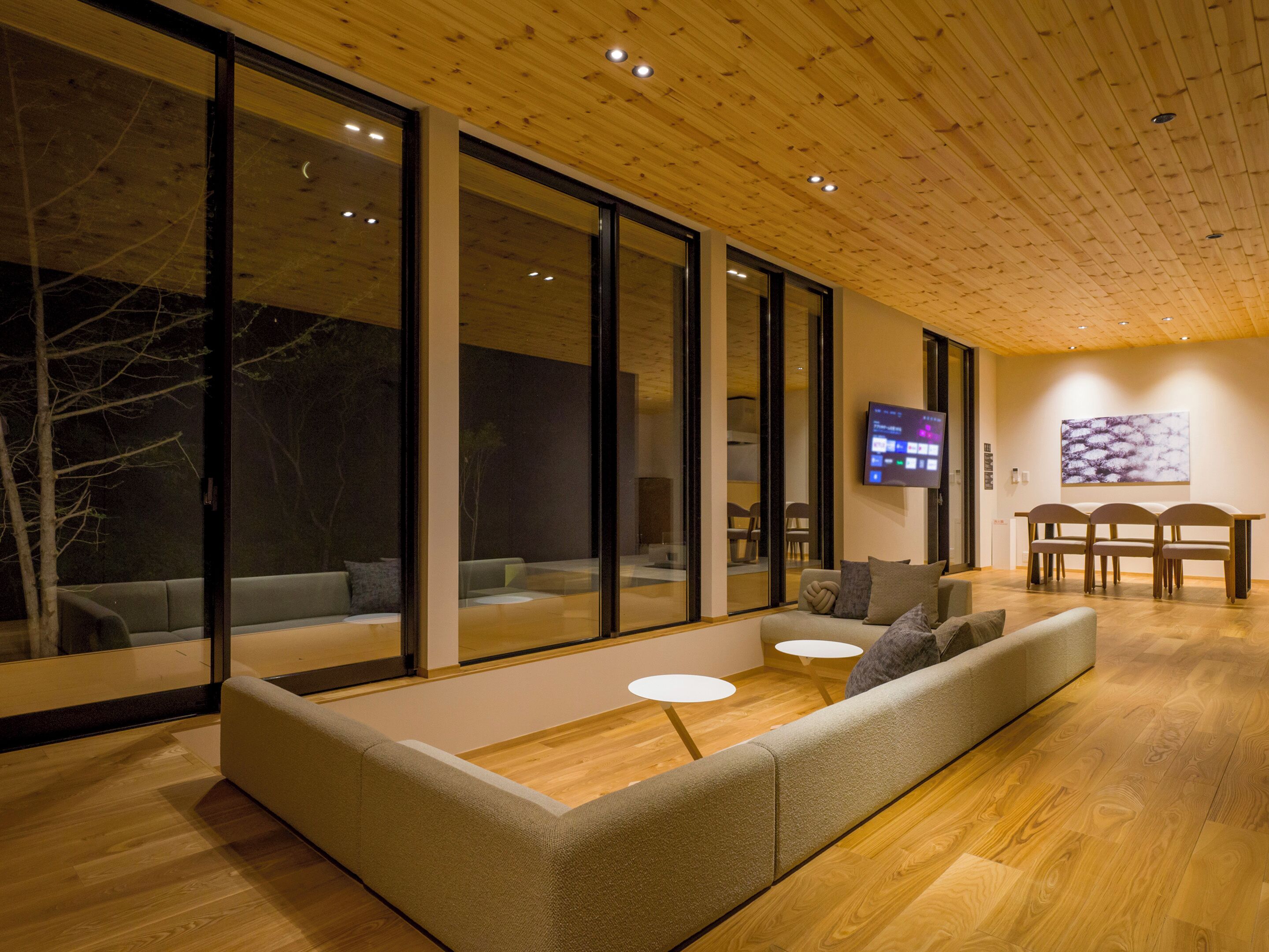 Un interior moderno con techo de madera, ventanas de vidrio amplias, un sofá y un televisor.