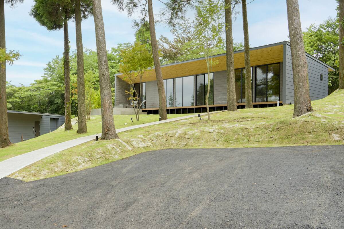 A modern building with large windows, surrounded by trees and a paved path.