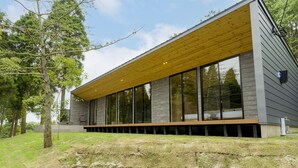 A modern building with large windows, a wooden overhang, and a grassy area with trees. - Rakuten STAY VILLA Aso Kurokawa (Minamioguni)