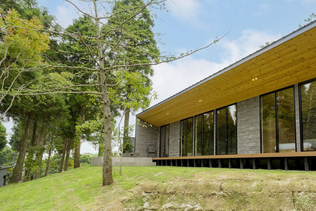 A modern building with large windows, a wooden overhang, and a grassy area with trees.