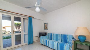 Une pièce comprenant un canapé, un téléviseur, un ventilateur de plafond et une fenêtre avec des rideaux.