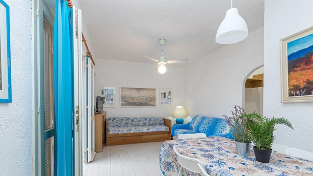 Une pièce comprenant un lit, un canapé, une table à manger avec des chaises, un ventilateur de plafond et une plante en pot.