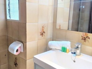 A bathroom with beige tiles, a toilet paper holder, a sink with a mirror, and toiletries. - Cala Benidorm by Interhome (Benidorm)
