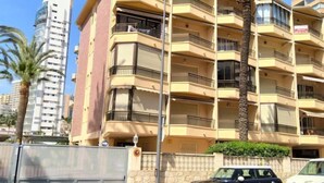 Un immeuble résidentiel à plusieurs étages, doté de balcons, d’un palmier et d’une voiture garée.