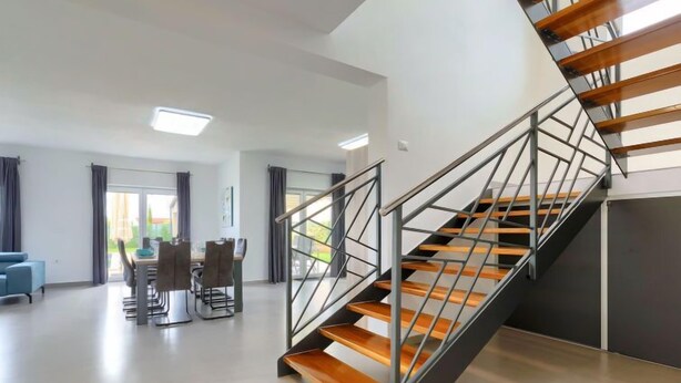 Un intérieur moderne avec un escalier, un coin repas et une vue à travers une porte vitrée.