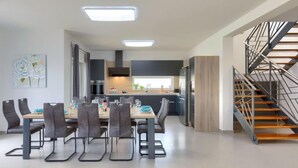 Une cuisine moderne avec des meubles de couleur sombre, un îlot central et un escalier doté d’une rampe en métal.
