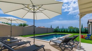 Un espace aménagé au bord de la piscine, avec des chaises longues et des parasols, une piscine et une vue sur le paysage environnant.