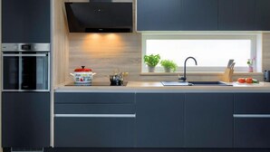 Une cuisine moderne avec des meubles de couleur sombre, un four encastré, une fenêtre ornée de plantes et un évier.