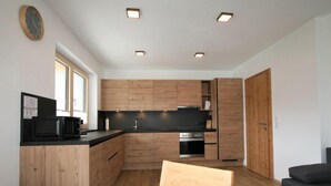 Una cucina moderna con mobili in legno, un piano di lavoro nero ed elettrodomestici integrati. C'è un tavolo da pranzo con una sedia e un divano nella zona soggiorno.