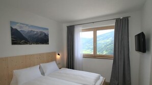 Una camera da letto con un letto, un quadro raffigurante montagne, una finestra con tende e un televisore appeso al muro.