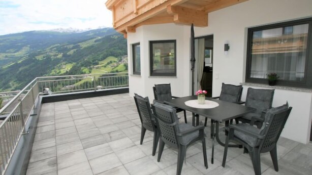 Una terrazza con tavolo e sedie, tetto in legno e vista su dolci colline e montagne.