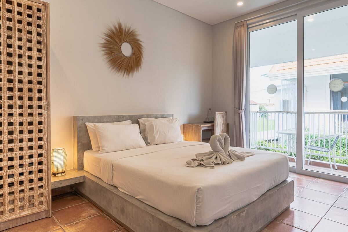 A spacious bedroom with a large bed, a decorative wall piece, and a view of the outside balcony.
