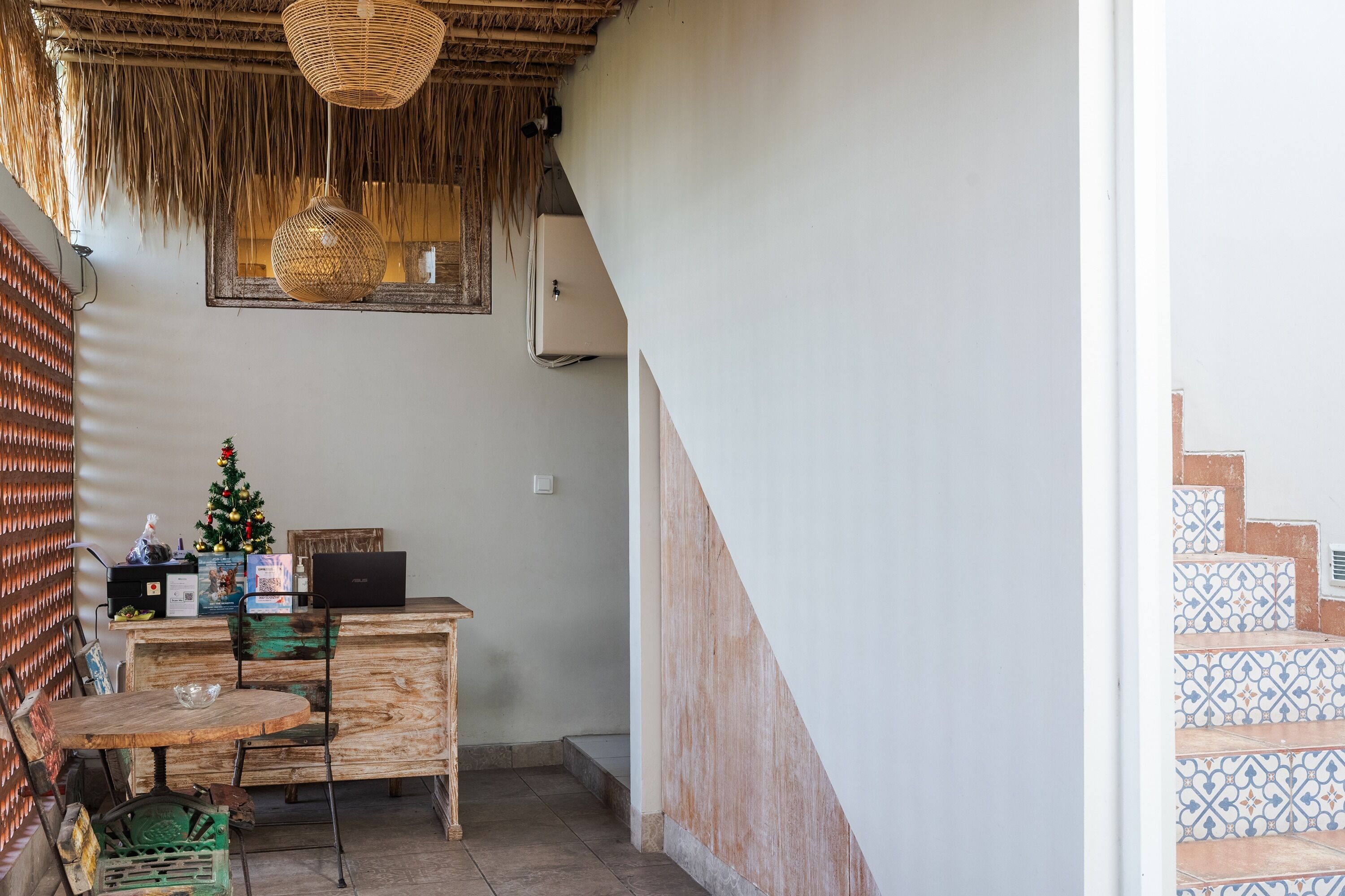 A wooden desk with a laptop, a small Christmas tree, and a wicker lamp.