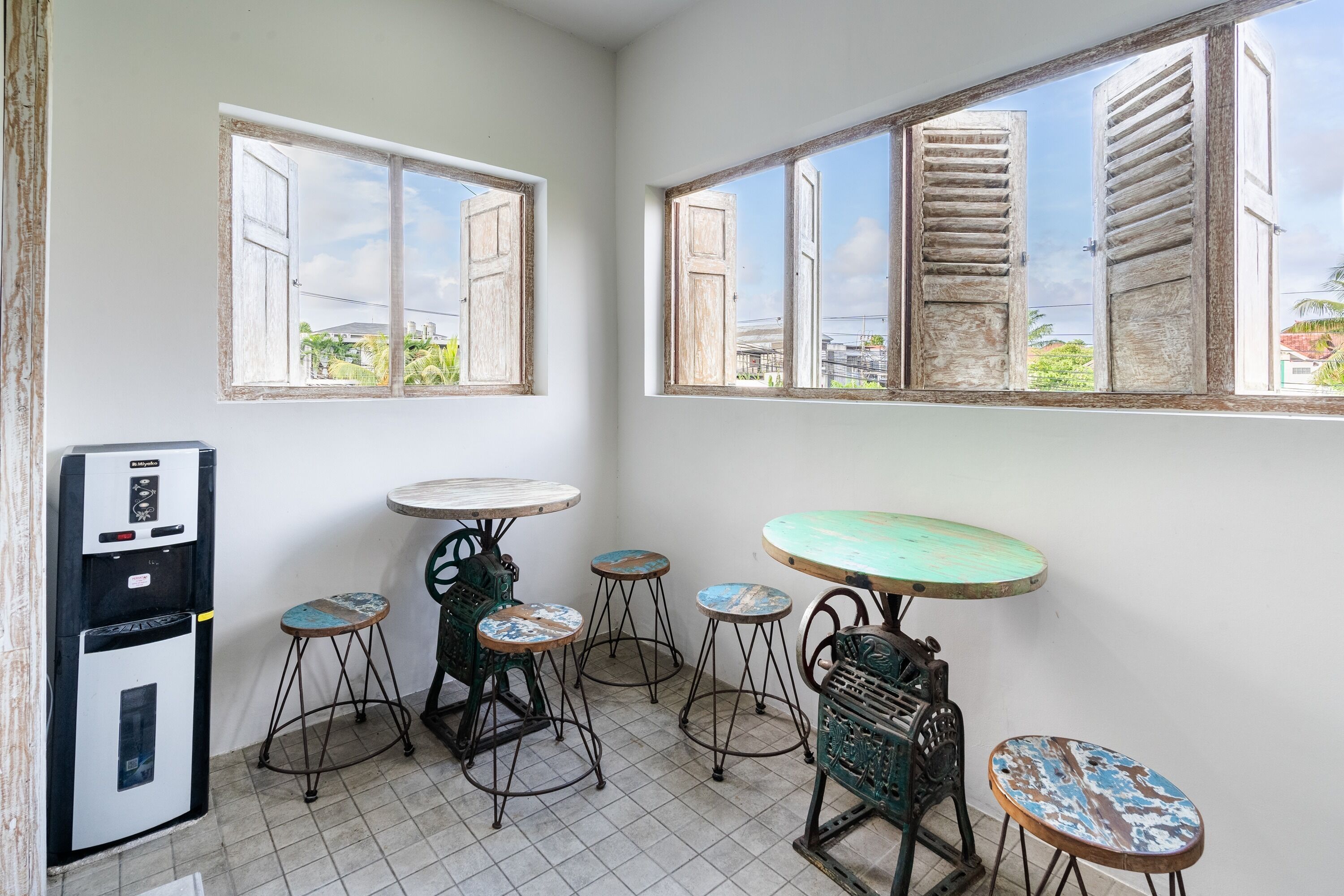 A kitchen with a refrigerator, a coffee machine, and a sink. There are four stools and a table.