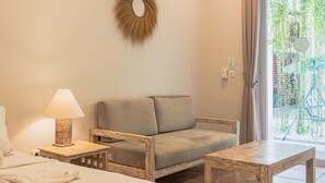 A cozy room with a wooden sofa, a small wooden table, a lamp, and a view of greenery outside. - Malam Hari ApartHotel (Canggu)
