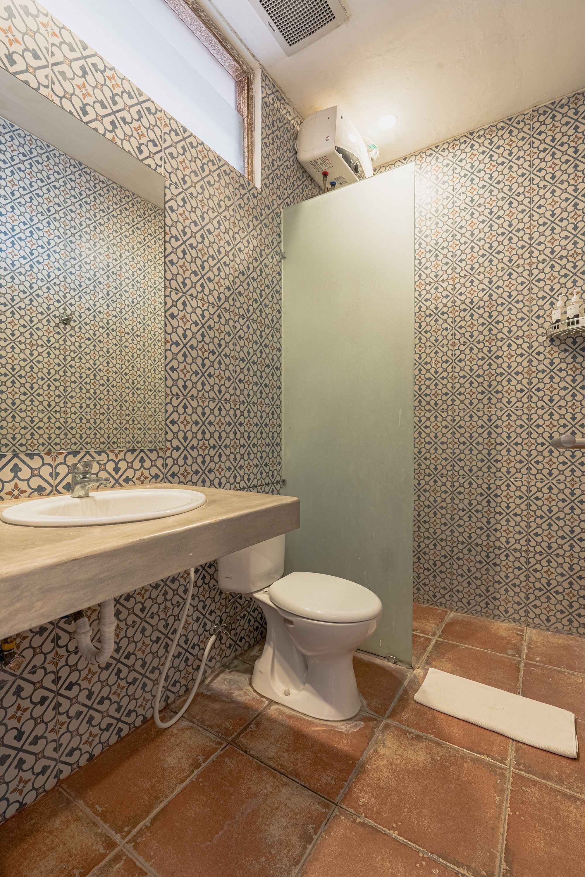 A bathroom with a patterned tile wall, a sink, a toilet, and a shower area.