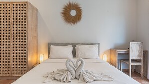 A neatly made bed with a heart-shaped towel arrangement, a wooden headboard, and a wall-mounted sunburst decoration. - Malam Hari ApartHotel (Canggu)