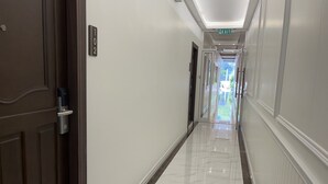 Un pasillo de hotel con piso de mármol, una puerta con placa de número y señal de salida.